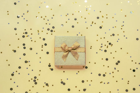 Gift in golden box on yellow background with confetti. Holidays concept. Top view, flat lay.の写真素材