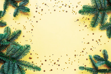 Fir branches and confetti on yellow background. Christmas concept. Top view, flat lay, copy space.