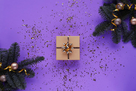 Fir branches, gift in a box and baubles on purple background with confetti. Christmas concept. Top view, flat lay.の写真素材