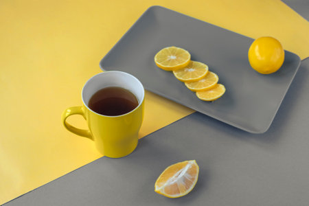 Yellow cup of tea and sliced lemon on gray plate. Trendy colors 2021.の写真素材