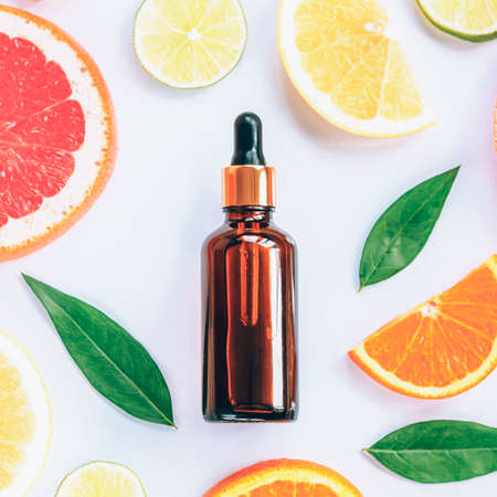 Glass bottle with cosmetic serum and sliced citrus fruits on white background. Natural cosmetics with vitamin C. Top view, flat lay.の写真素材
