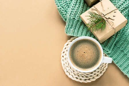 A cup of coffee and Christmas gifts on green sweater on beige background. Top view, flat lay, copy space.の写真素材