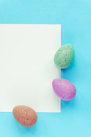 Three painted eggs and blank sheet on blue background, top view, flat lay. Easter concept.の写真素材