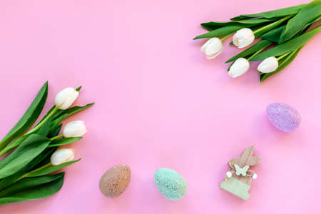 Easter festive background with painted eggs, wooden toy rabbit and white tulips on pink. Top view, flat lay, copy space.の写真素材