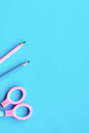 Two wooden pencils and scissors on pink and blue colored paper background. Education concept. Top view, flat lay, copy space.の写真素材