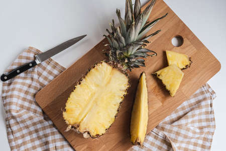 Fresh pineapple on a cutting board with textile napkin on a white table, top view.