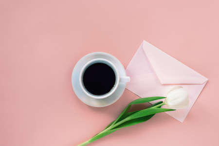 Cup of coffee, envelope and white tulip on coral pink background. Womens day or Mothers day concept....