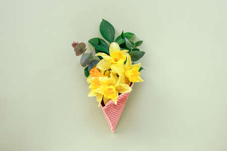 Bouquet of yellow daffodils in a waffle cup light green background. Spring concept. Top view, flat...