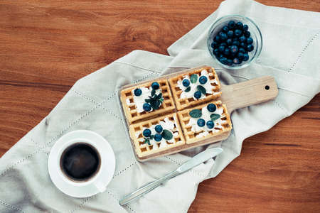 Waffles with cream and blueberries, a cup of coffee on the table on a cloth napkin. Breakfast concept. Top view, flat lay.の写真素材