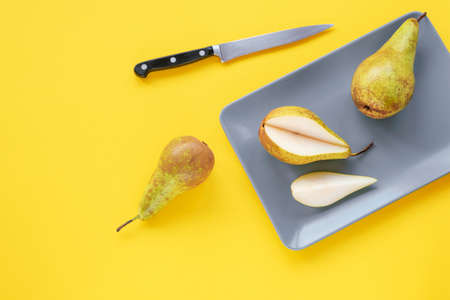 Ripe pears on gray plate and knife on a yellow background, top view, flat lay.
