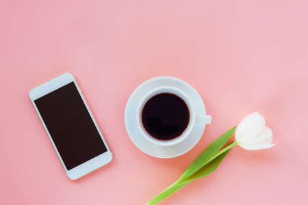 Cup of coffee, phone and white tulip on pink background. Women's day or Mother's day concept. Top...