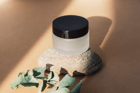 Cream jar, natural skin care product on natural stone podium with eucalyptus branch in sunlight. Beige background. Mock upの写真素材