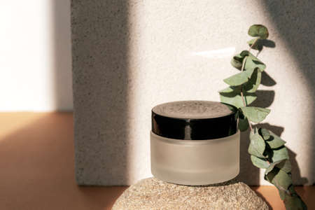 Cream jar, natural skin care product on natural stone podium with eucalyptus branch in sunlight. Beige background. Mock upの写真素材