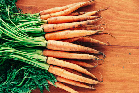 Carrot with green leaves on orange wooden table, top view, flat lay