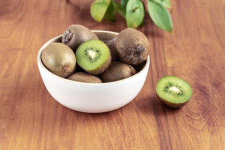 Kiwi fruits in a white bowl on wooden table. Healthy vegan food. Close up.の写真素材