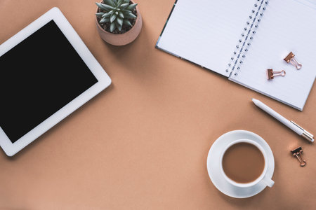 Overhead workplace with tablet computer, notepad, pen, coffee cup and succulent plant on beige background. Top view, flat lay, copy space.の写真素材