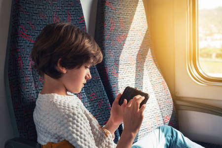 Ten year old girl playing games on the phone on a train on a sunny day.