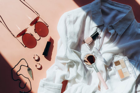 Feminine summer fashion flat lay with blouse, sunglasses, earrings, chain with a pendant and cosmetics on pink background in sunlight. Top view, flat lay.の写真素材