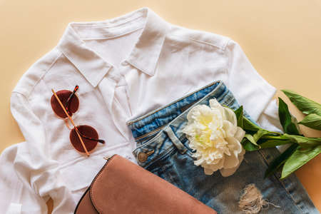 Feminine summer fashion flat lay with blouse, handbag, sunglasses and white peony flower on beige background. Stylish summer clothes, beauty concept. Top view, flat layの写真素材