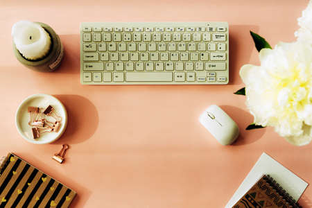 Woman workplace with peony flowers, notepad, candle, computer keyboard and computer mouse. Top view, flat lay. Pink background.の写真素材