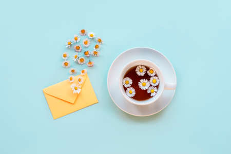 A cup of chamomile tea, an envelope and daisy flowers on blue background. Top view, flat lay, copy spaceの写真素材
