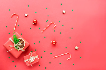Christmas and New Year holiday background. Gift boxes with confetti, balls and baubles on red background. Top view, flat lay, copy spaceの写真素材