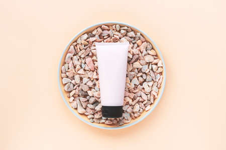 Cosmetic unbranded cream tube on natural stones on beige background. Top view, flat lay. Mock up.