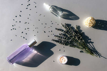 Lavender flowers and hydrolat, serum in glass bottles, cream jar on light gray background, top view. Aromatherapy and natural cosmetics concept. Flat lay, copy space.の写真素材