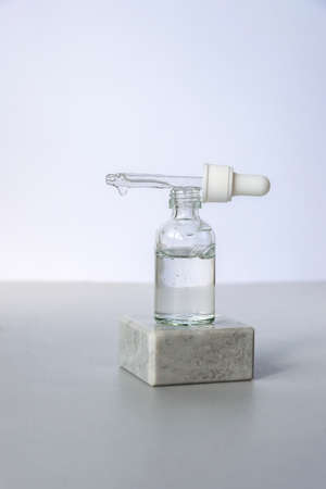Bottle of natural skincare lotion with pipette on podium on light grey background. Trendy selfcare products. Front view.の写真素材