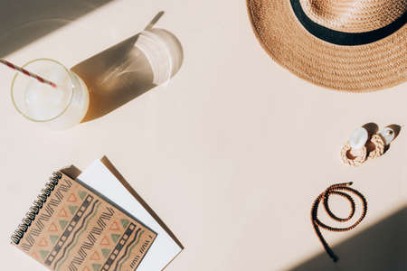 Desktop with notepad, fresh lemonade with ice cubes, hat and earrings on beige background. Summer vacation concept, top view, flat lay, copy spaceの写真素材