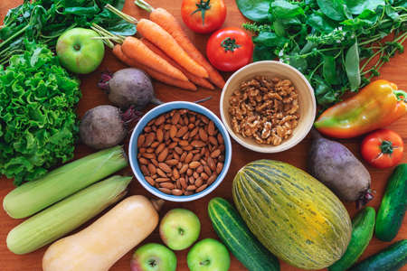 Organic fresh vegetables, almonds and walnuts. Vegan healthy raw food on wooden table background. Top view, flat layの写真素材