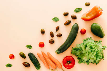 Zucchini, avocado, tomato, carrot, cucumber, bell peper and lettuce on beige background. Healthy raw vegan food, diet, detox concept. Top view, flat lay, copy spaceの写真素材