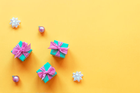Three turquoise present boxes with pink bows, Christmas balls and baubles on yellow background. Top view, flat lay, copy space.の写真素材