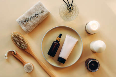 Cosmetic layout with serum bottle, cream tube, wooden brushes, candles and towel on beige background. Selfcare, home spa and relaxation concept. Flat lay, top view.の写真素材