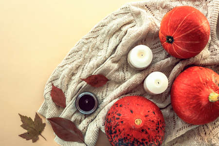 Autumn flat lay with pumpkins, leaves, candles on a knitted sweater. Beige background, top view.