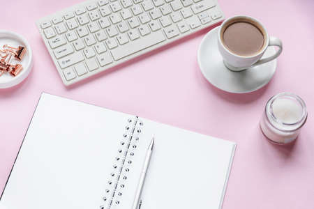 Cozy workplace with blank notepad, keyboard, cup of coffee and candle. Top view, flat lay. Pink background.の写真素材