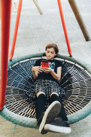 Teenage girl using mobile phone on the children's swing in the park.の写真素材