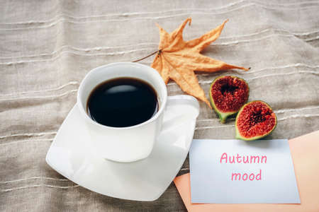 Coffee in a white cup, figs and an autumn leaf. Orange envelope, words Autumn mood. Still lifeの写真素材