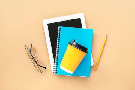 Tablet computer, blue notepad, glasses and yellow coffee cup on the table. Study concept. Top view,...
