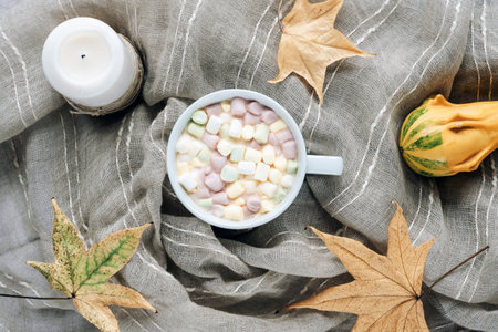 Cup of cocoa with marshmallows on a gray textile background with autumn leaves, pumpkin and candle. Top view, flat lay.の写真素材