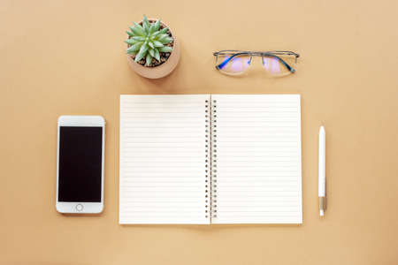 Blank notepad, pen, smartphone, glasses and potted plant on beige table. Top view, flat lay, mock up.の写真素材