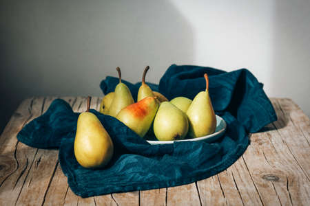 Fresh ripe pears on a plate with kitchen cloth napkin on wooden table. Healthy vegan food. Close up.の写真素材