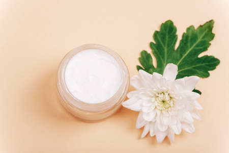 Natural cosmetics cream jar and white dahlia flower on beige background. Top view, selective focus.の写真素材