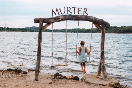 Girl swinging on a wooden swing against the background of the sea. Murter, Croatia.の写真素材
