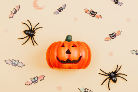 Halloween pumpkin Jack O Lantern, spiders and bats on light orange background. Top view, flat lay, copy spaceの写真素材