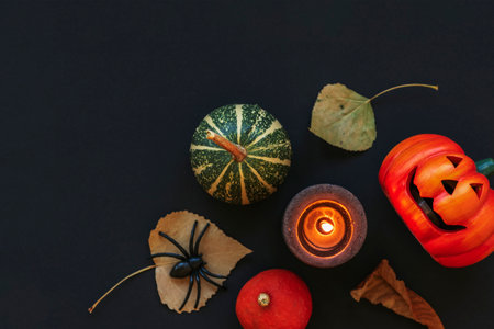 Halloween festive flat lay with Jack-O-Lantern, pumpkins, candle, dry leaves and spider on black table. Autumn holidays concept. Top view, copy space.の写真素材
