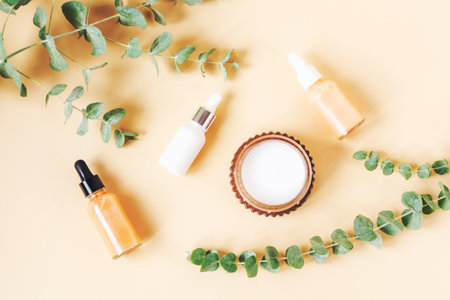 Cosmetic dropper bottles, aroma candle and eucalyptus branches on beige background. Natural cosmetics, aromatherapy and skin care concept. Top view, flat lay.の写真素材