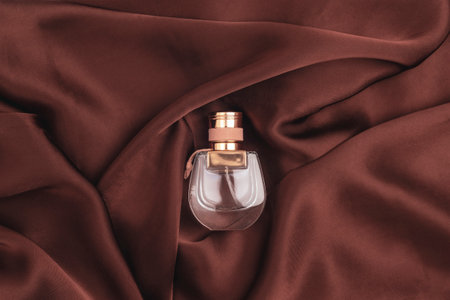 Perfume bottle on brown satin fabric. Top view, flat lay.