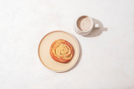 Bun on a plate and coffee with milk on a white table. Breakfast concept, harsh shadows. Top view, flat lay.の写真素材