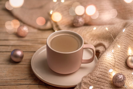A cup of hot drink and Christmas balls on a knitted sweater, decorated with a garland lights. Winter holidays concept.の写真素材